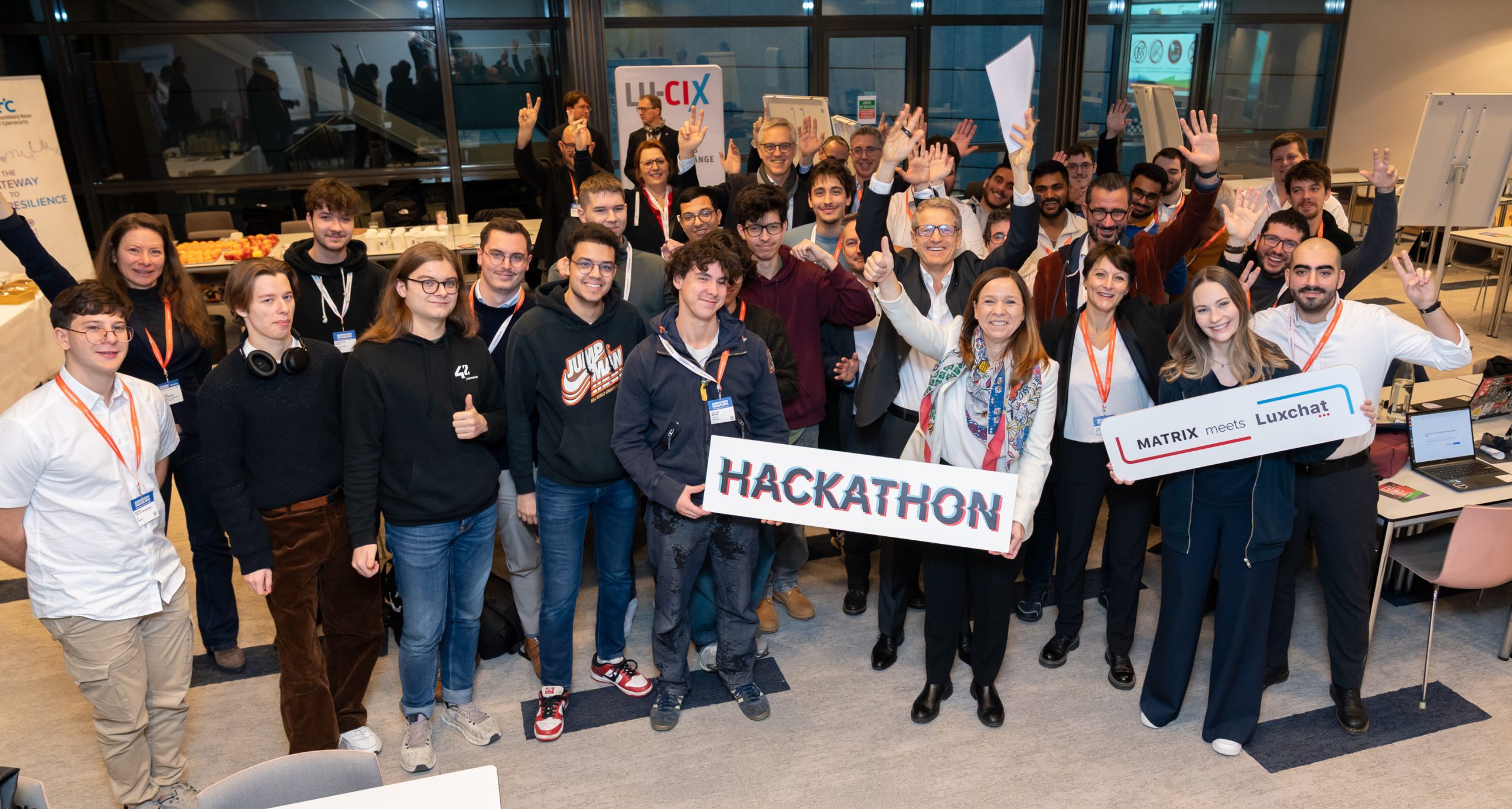A picture of a crowd holding two signs. One reads "Hackathon" and the other "Luxchat meets Matrix"